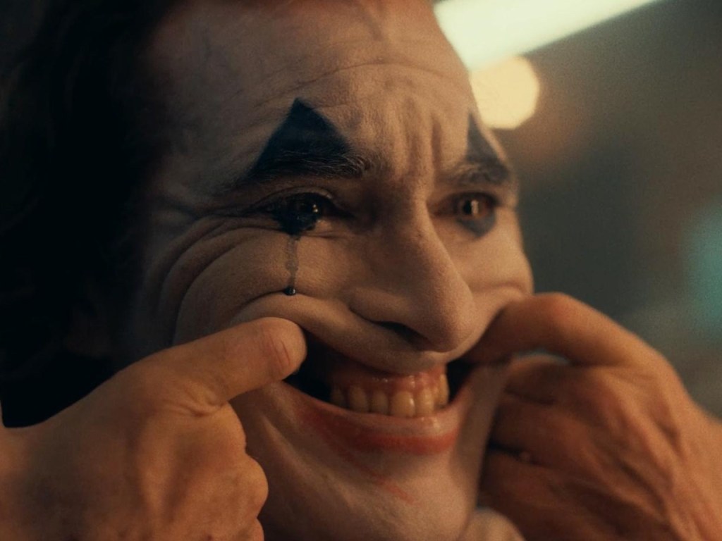PArmaklarını ağzına sokarak kendini zorla gülümseten joker
